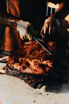 close up photo of a person wearing hand gloves cutting roasted meat